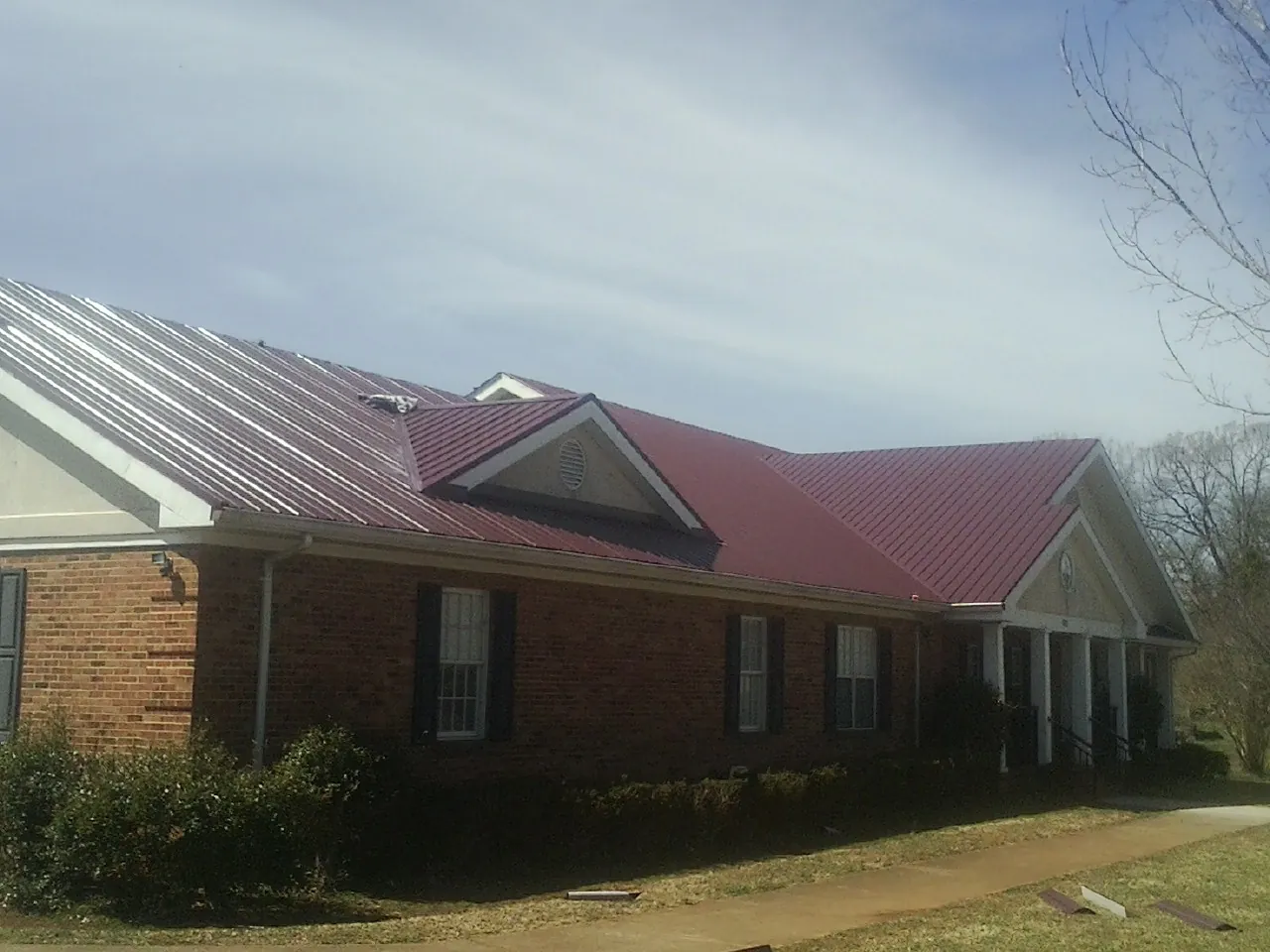 Red metal roof with gabled entries on a long brick building, from a Hail Damage Roof Repair job in Cornwall Bridge