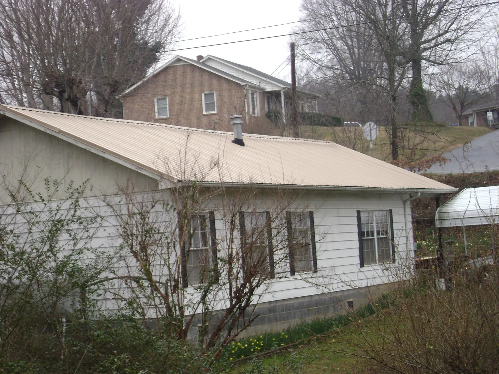 Tan metal roof on a white sided house set into a hillside — Commercial Roofing by Roofing Brothers in Cornwall Bridge